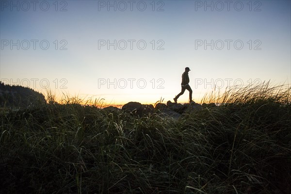 Silhouette of distant Caucasian man walking on rocks at sunset