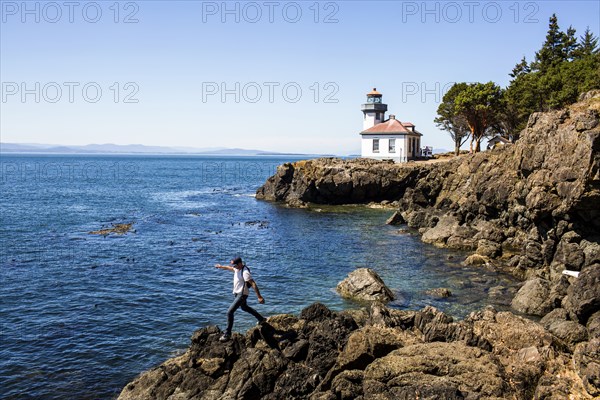 Caucasian man walking on rocks near lighthouse