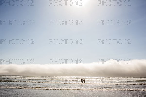 Caucasian mother and son wading in ocean waves at beach