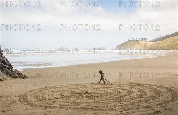 Caucasian girl drawing circles on beach with stick