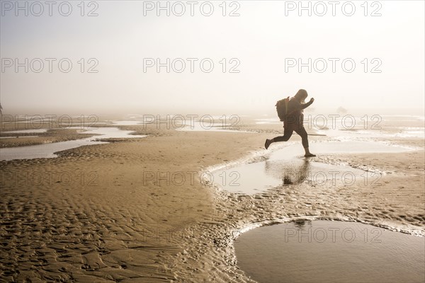 Caucasian mother carrying daughter jumping over puddle at beach