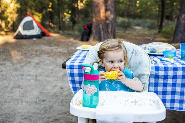 Caucasian girl eating corn in high chair