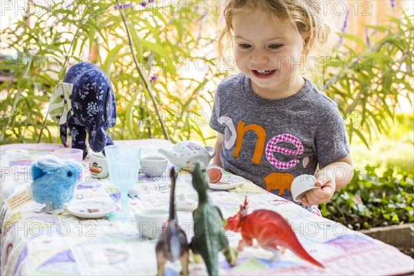 Caucasian girl playing with tea set and dinosaurs