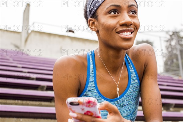 Smiling Black woman sitting on bleachers texting on cell phone