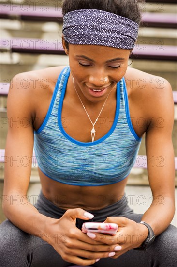 Smiling Black woman sitting on bleachers texting on cell phone