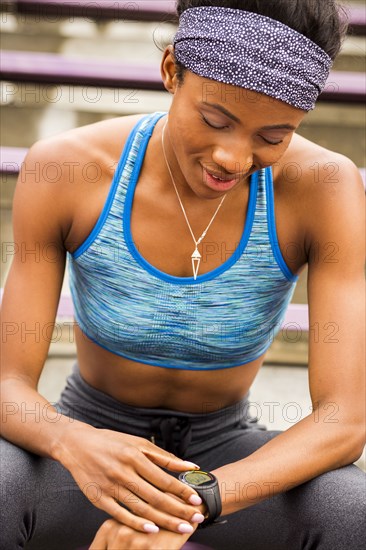 Black woman sitting on bleachers checking smart watch