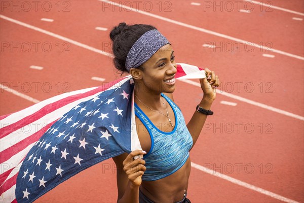 Smiling Black athlete holding American flag on track