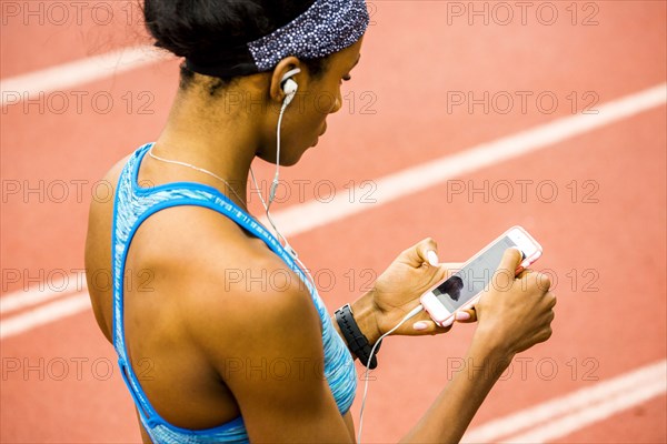 Black woman on track listening to cell phone with earbuds