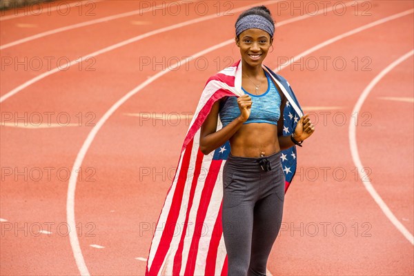 Smiling Black athlete posing with American flag on track