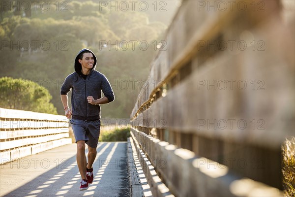 Smiling Mixed Race man running on footbridge