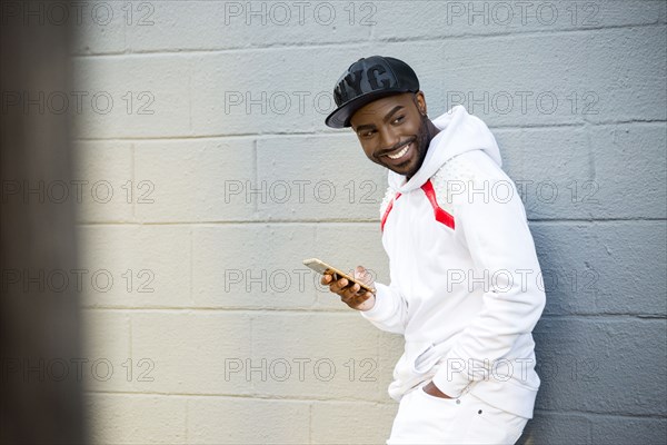 Smiling Black man leaning on wall holding cell phone