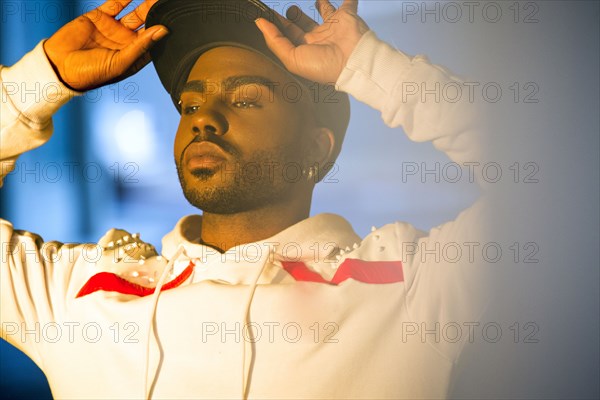 Serious Black man holding brim of baseball cap