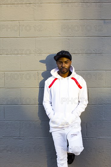 Serious Black man leaning on gray wall