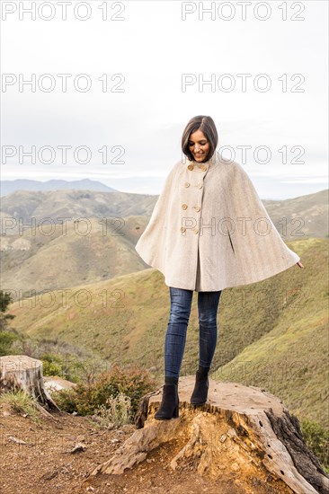 Smiling Indian woman wearing poncho standing on tree stump