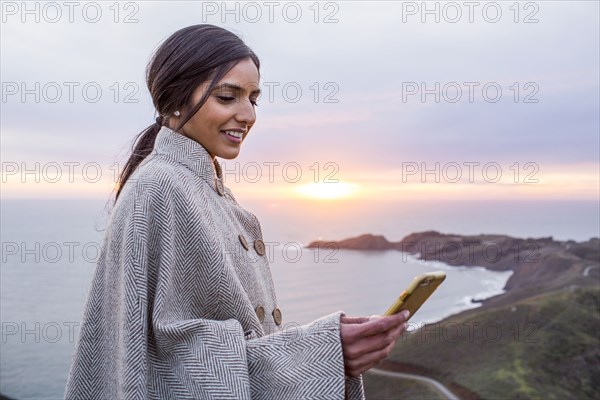 Smiling Indian woman texting on cell phone near shore