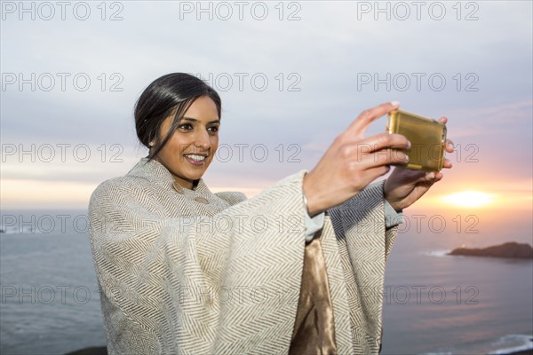 Indian woman posing for cell phone selfie near ocean