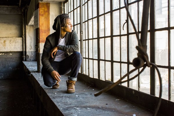 Androgynous Mixed Race woman crouching near window