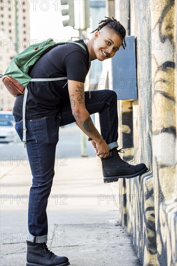 Androgynous Mixed Race woman carrying backpack adjusting boot