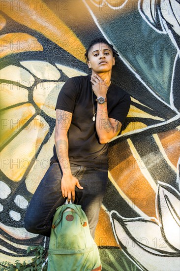 Portrait of androgynous Mixed Race woman leaning on graffiti wall