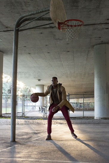 Black man wearing backpack playing basketball under overpass