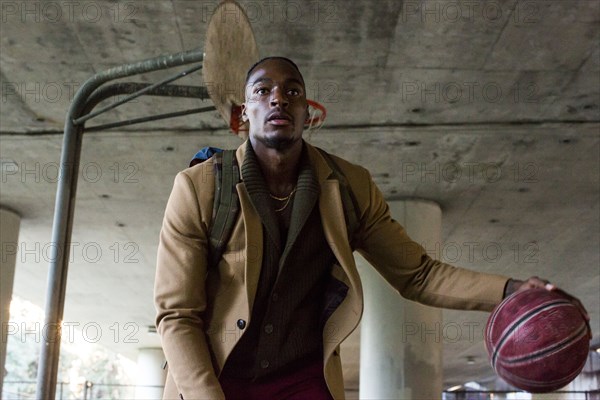 Black man wearing backpack playing basketball under overpass