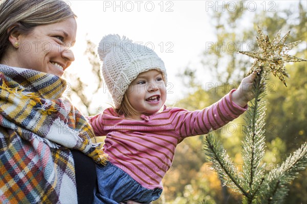 Caucasian mother helping daughter place star on top of Christmas tree