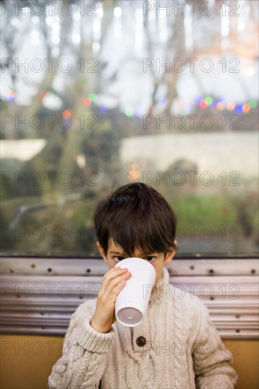 Mixed Race boy drinking from cup near train window