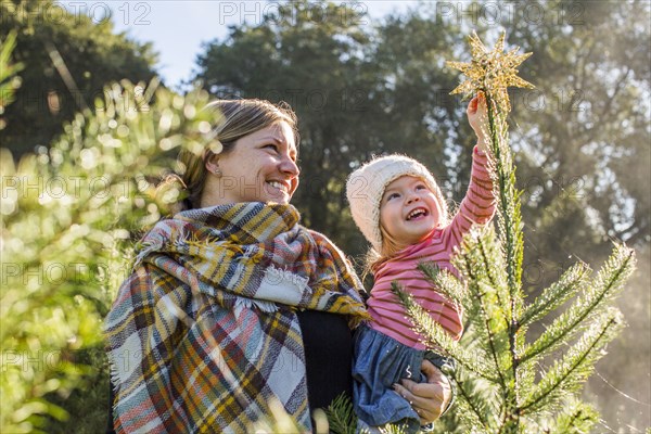 Caucasian mother helping daughter place star on top of Christmas tree