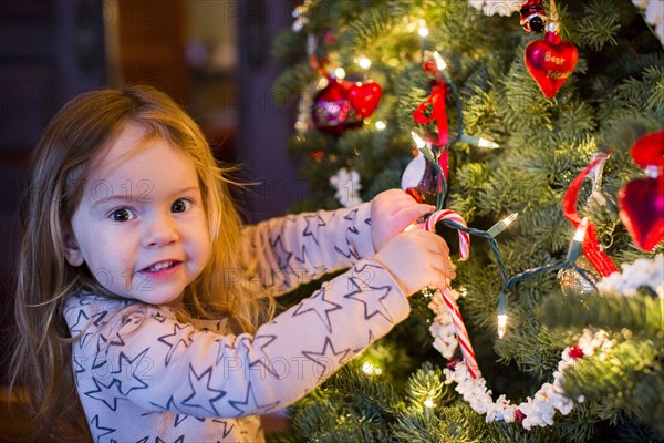 Caucasian girl hanging candy cane on Christmas tree