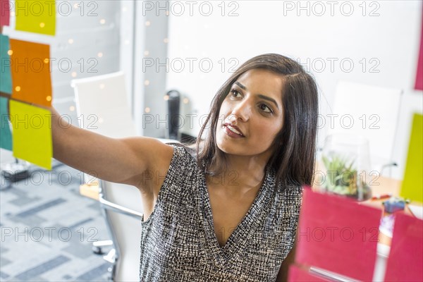 Indian woman reading adhesive notes in office