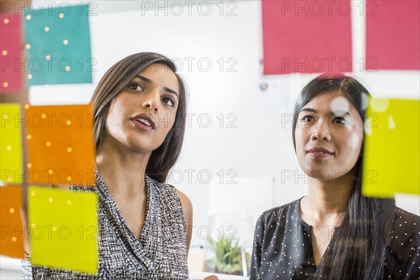 Women reading adhesive notes in office