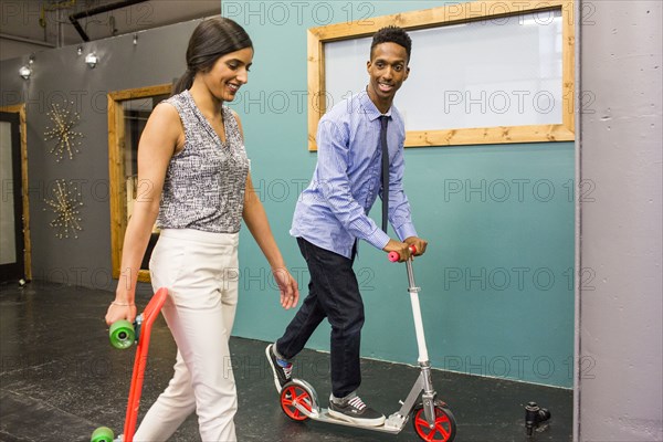 Man and woman with skateboard and scooter indoors