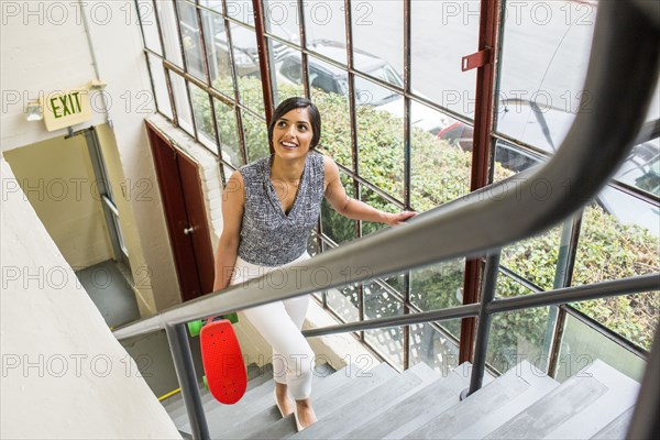 Asian woman carrying skateboard on staircase