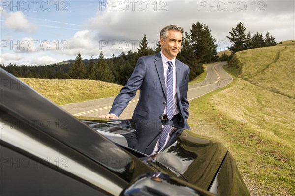 Smiling Caucasian businessman leaning on car