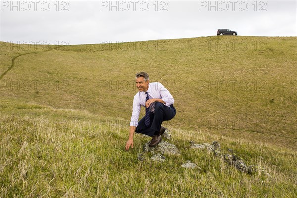 Smiling Caucasian businessman crouching in grass