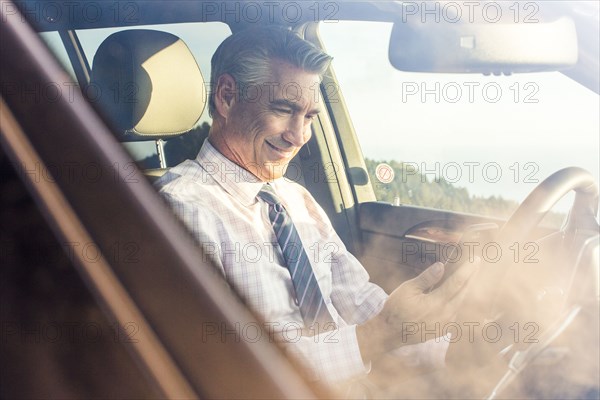 Smiling Caucasian businessman sitting in car texting on cell phone