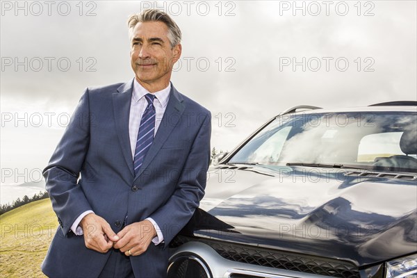 Smiling Caucasian businessman leaning on car