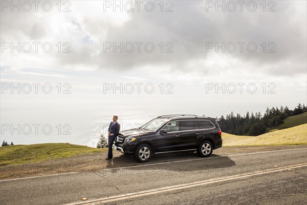 Distant Caucasian businessman leaning on car