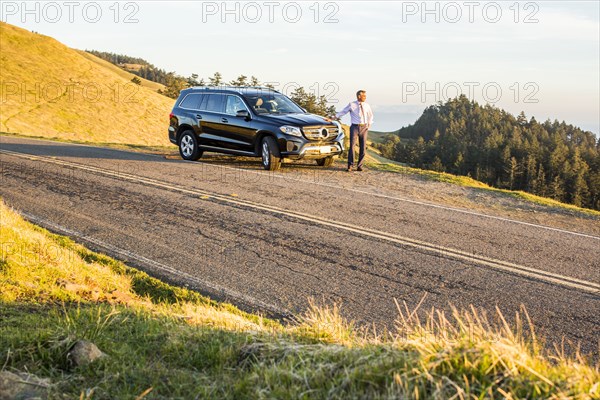 Distant Caucasian businessman leaning on car