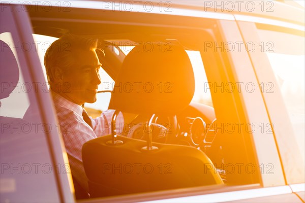 Smiling Caucasian businessman driving car on sunny day