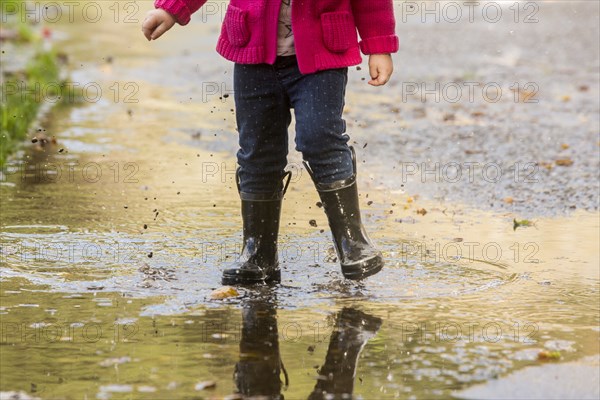 Caucasian girl wearing boots splashing in puddle