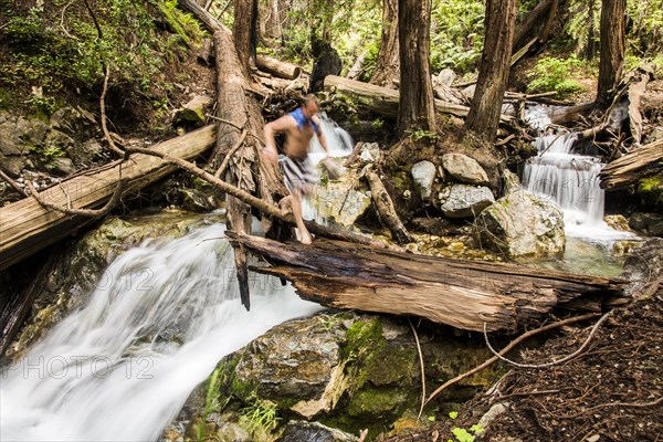 Caucasian man walking over waterfall on log in woods