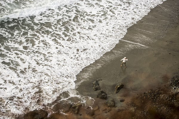 Distant Caucasian woman throwing stone on ocean beach