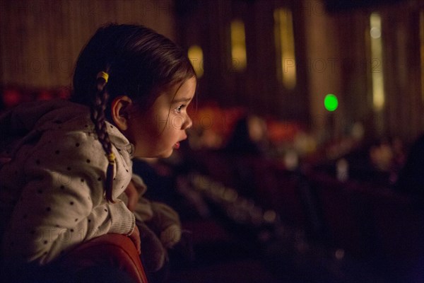 Mixed Race girl leaning on chair watching movie in theater