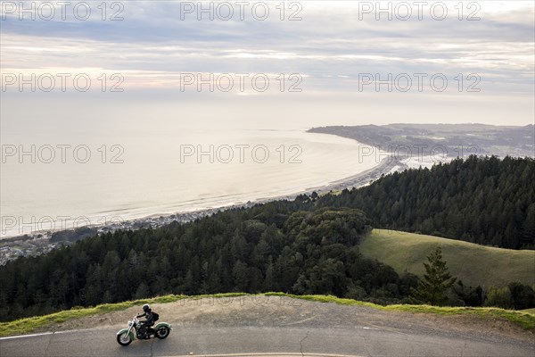 Person riding motorcycle at edge of cliff near ocean