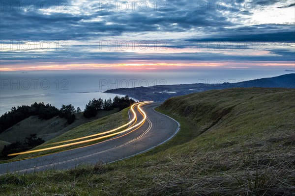 Light trails on winding road near ocean