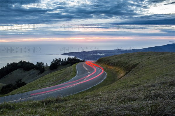 Light trails on winding road near ocean