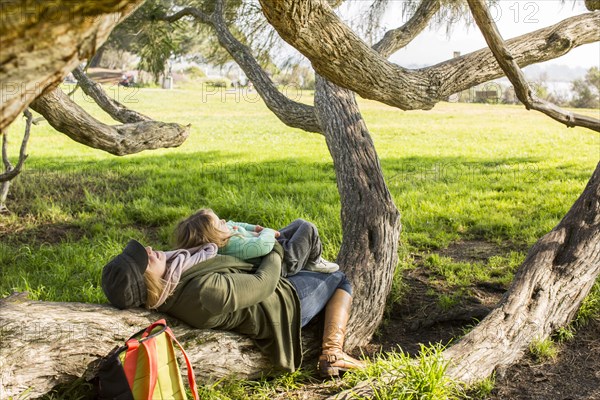 Caucasian mother and daughter laying on tree branch