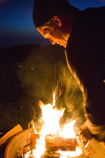 Caucasian man stoking campfire at night