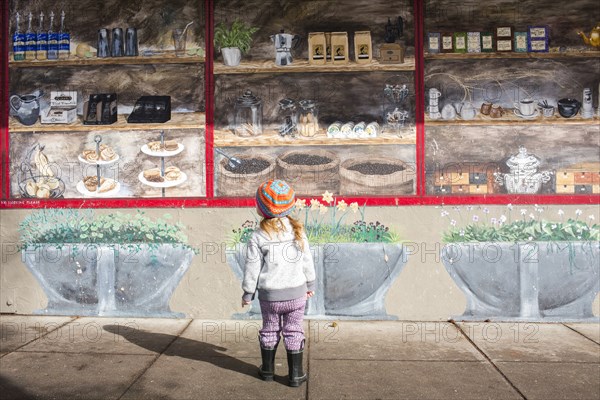 Caucasian girl standing on sidewalk admiring mural on wall